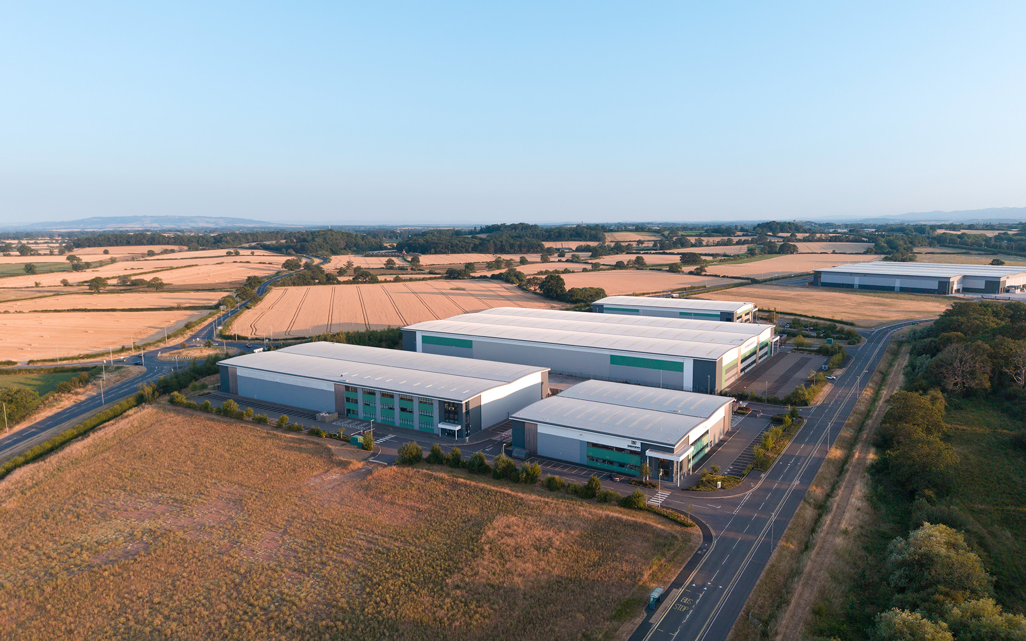 Aerial View of Modern Industrial Warehouse Complex in Green Countryside at Sunset
